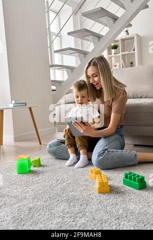 Smiling mum teaching toddler child son using digital tablet at home. Stock Photo