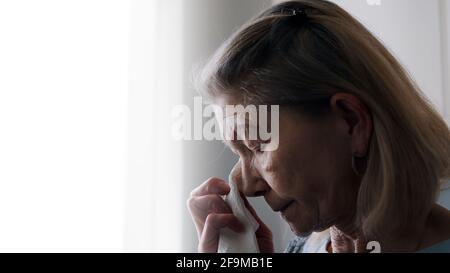 Depressed old lonely woman wiping tears with tissue while looking through the window. High quality photo Stock Photo