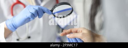 Dermatologist doctor looking at patients skin on hands using magnifying glass in clinic closeup Stock Photo