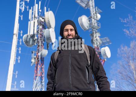 Professional shot of a young man standing in front of blurred out telecommunication towers used for cellular signals transmission. Stock Photo