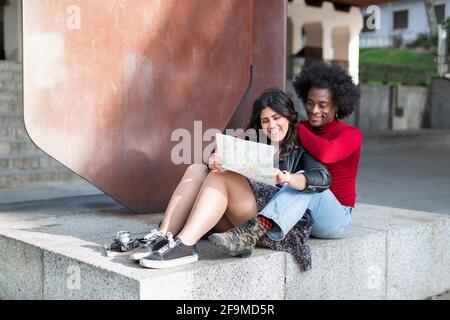 Young multiracial couple on vacation having fun in the city. They are sitting while looking at a tourist map. Urban travel concept. Space for text. Stock Photo