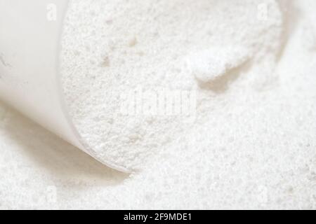 Macro image of clear plastic scoop measuring out white laundry detergent powder. Domestic cleaning chemical for clothing and fabrics. Stock Photo