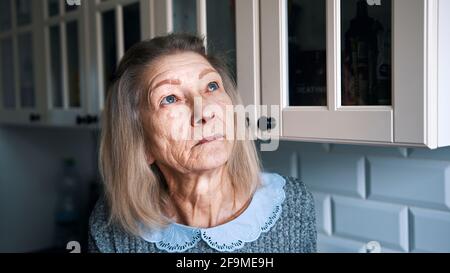 Sad lonely old gray haired woman looking through the window. Vulnerable person in quarantine. High quality photo Stock Photo