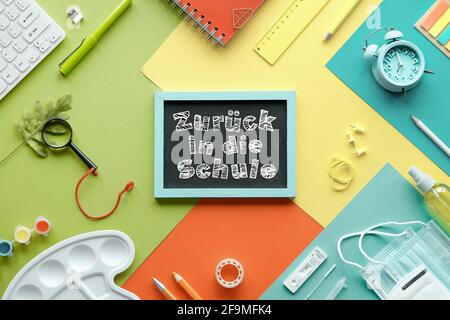 Zuruch in die Schule means or back to school in German language. Concept top view with chalk text on blackboard. Corona quick tests, mask, stationary Stock Photo