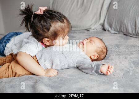 Cute toddler older sister hugging newborn younger baby brother boy. Stock Photo