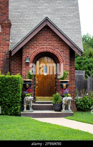 Cute little brick cottage entrance decorated  for party with beads on bear statues and colorful flowers and party lights around arched wooden door Stock Photo
