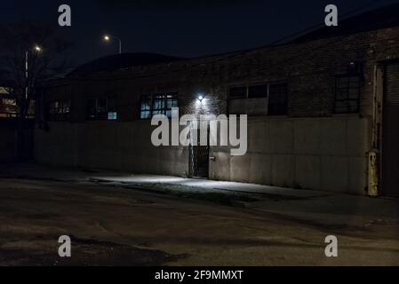 Dark scary alley at night with gated door warehouse entrance Stock Photo