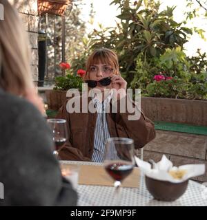 A woman sit down in a cafe with her friend, she is looking bruise’s friend. is holding sunglasses Stock Photo