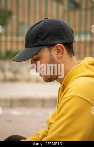 Portrait of a young male wearing a yellow hoodie and black cap in a street Stock Photo