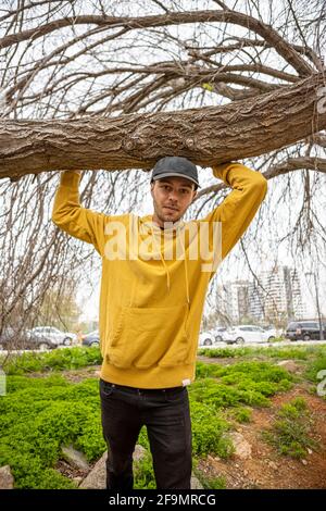 Young cmale in a yellow hoodie touching a dry tree in the background  Stock Photo