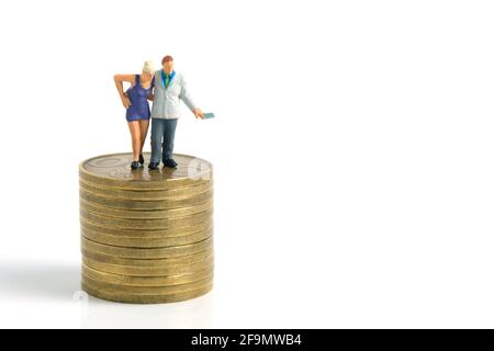 Miniature tiny people toys photography. a generous man standing on a pile of coins, giving money cash, isolated on white background. Stock Photo