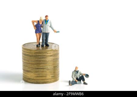Miniature tiny people toys photography. a generous man standing on a pile of coins, giving money cash to a beggar poor man, isolated on white backgrou Stock Photo