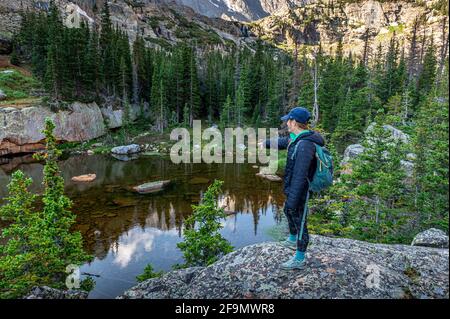 Hiker pointing down at the shallow Embryo Lake in the Loch Vale Stock Photo