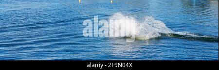 Man learning to wakeboard at a cable ski park and not succeeding as he falls off with a splash Stock Photo