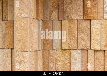 Corner view of a modern rough textured limestone wall background with vertical aligned natural stone bricks in varying widths and shades of beige Stock Photo