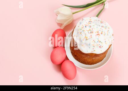 Easter cake on a plate with a tulip flower and colorful Easter eggs on the pink background. Traditional orthodox christian easter food. Top view. Stock Photo