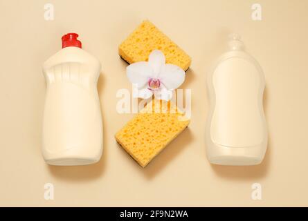 Bottles of dishwashing liquid and sponges on a beige background. Stock Photo