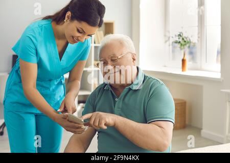 Friendly doctor teaching senior man to use special health indicator mobile app Stock Photo