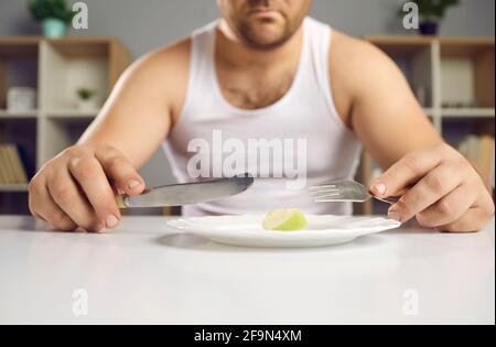 Cropped view sad man on diet holding cutlery near plate with small apple piece Stock Photo