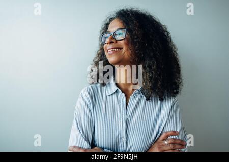 Close-up of a happy mature businesswoman looking away and smiling. Female executive in formal shirt standing against a while wall in office. Stock Photo
