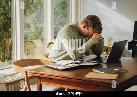 Man feeling stressed while working on laptop. Man sitting at table looking down with hand on head. Stock Photo