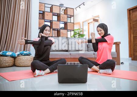 two Muslim women in sports clothes sit warming up with one hand holding the other hand when one hand is pulled to the side Stock Photo