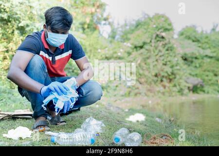 Frontline healthcare worker or waste collector busy collecting discarded medical or PPE waste from near by lake or river during coronavirus covid-19 Stock Photo