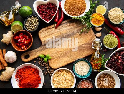 Various spices in a bowls and empty cutting board on black concrete background. Top view copy space. Stock Photo