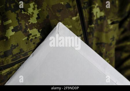 Large mailing bag on camouflage fabric. Sealed paper envelope with documents inside against a military jacket. Closeup. Selective focus. Low key. Stock Photo