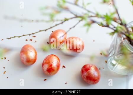 Easter light still life with spring twigs with delicate greens, red and gold eggs on a white table. Stock Photo