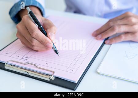 business man works on the table holds pen in right hand and write data in the table chart, wear a white and blue shirt. Stock Photo