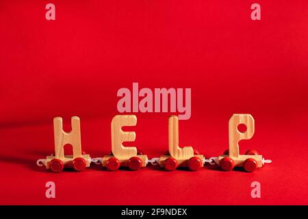 Wooden train made of letters Help on red backdrop. Humanitarian aid, shipping, material assistance, governmental help concept. Stock Photo