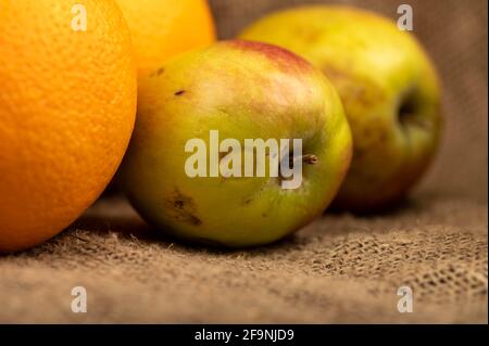 Fresh green apples and juicy oranges on a homespun fabric with a rough texture. Close-up selective focus. Stock Photo