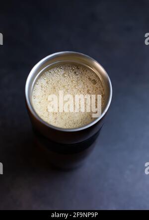 Coffee foam with vegetable oat milk at metal thermos cup on grey table, top view, hot breakfast drink Stock Photo