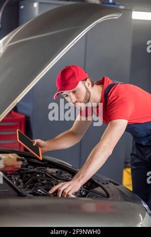 Auto mechanic with tablet examining car under hood Stock Photo