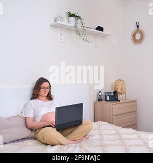 Happy pregnant woman working at computer in home bedroom interior Stock Photo