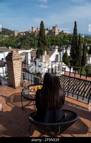 Back view of tourist woman sitting on terrace admiring views of Albaicin neighborhood and Alhambra of Granada, Spain Stock Photo