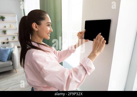 Woman using smart wall home control system in living room Stock Photo