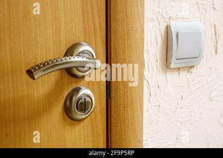 door handle on a wooden door near the wall with a switch indoor closeup Stock Photo