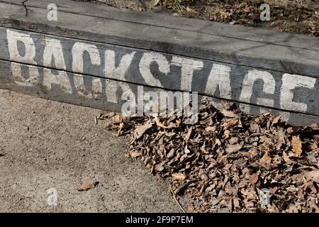 Diagonal white inscription 'backstage' on a street bench next to fallen leaves Stock Photo