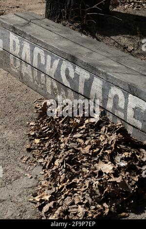 Vertical shot with diagonal white inscription 'backstage' on a street bench next to fallen leaves Stock Photo