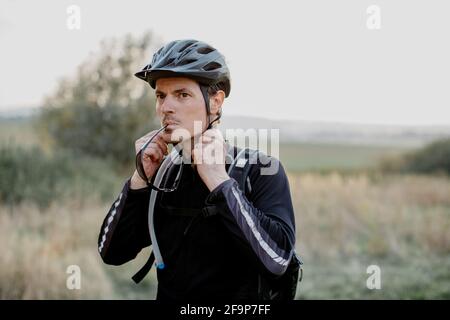 Man wearing sportswear putting helmet on. Male cyclist fastening helmet strap before setting off on bike trek. Stock Photo