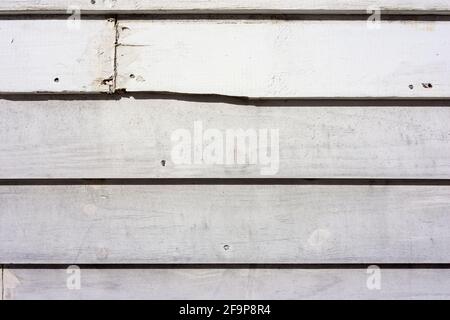 Old clapboard siding painted white with cracks and a broken board in the morning light. Stock Photo