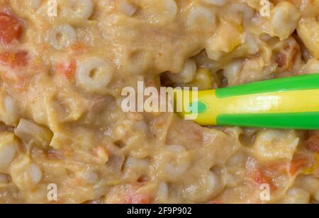 Close view of macaroni and cheese baby food with a spoon in the food illuminated with natural light. Stock Photo