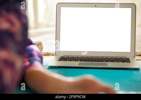 Woman using laptop and working out on yoga mat at home. Distant work. Healthy lifestyle and social media concept. White empty screen. Stock Photo