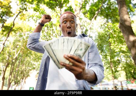 Big win concept. Excited African American guy holding fan of American money at park Stock Photo