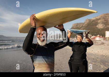 Portrait of senior african american couple carrying surf board on their head on the beach. travel vacation retirement lifestyle concept Stock Photo