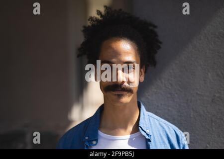 Portrait of mixed race male with moustache looking to camera. green urban lifestyle, out and about in the city. Stock Photo