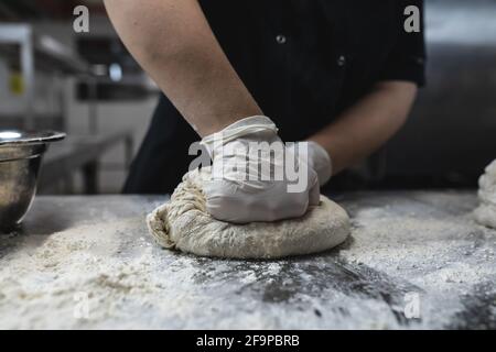 Midsection of professional chef preapring dough wearing sanitary gloves. working in a busy restaurant kitchen. Stock Photo