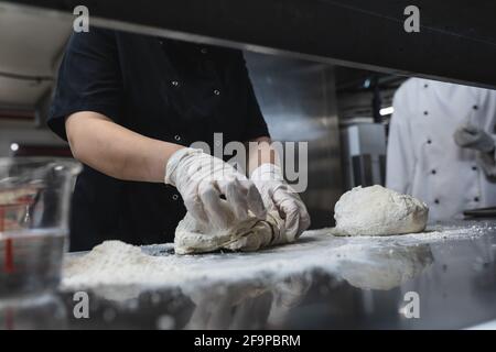 Midsection of professional chef preapring dough wearing sanitary gloves. working in a busy restaurant kitchen. Stock Photo